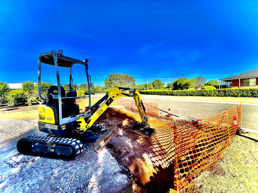 Riverina Diggers excavator cutting a driveway crossover behind orange safety fencing in Griffith
